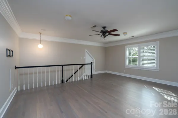 a view of an empty room with wooden floor and a ceiling fan