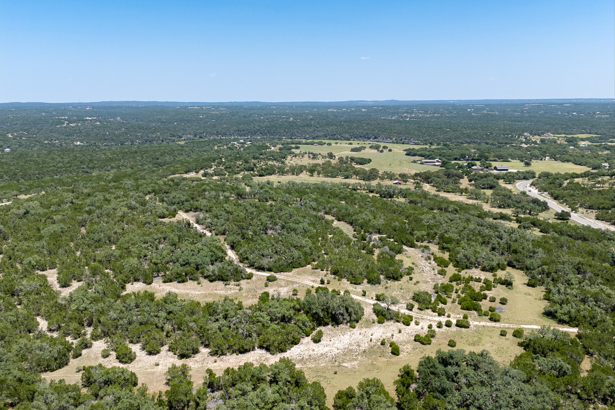 4698 Fischer Store Road Wimberley, TX 78676 - Photo 21 of 28 Lush wooded acreage rolls across the landscape under a clear blue sky.