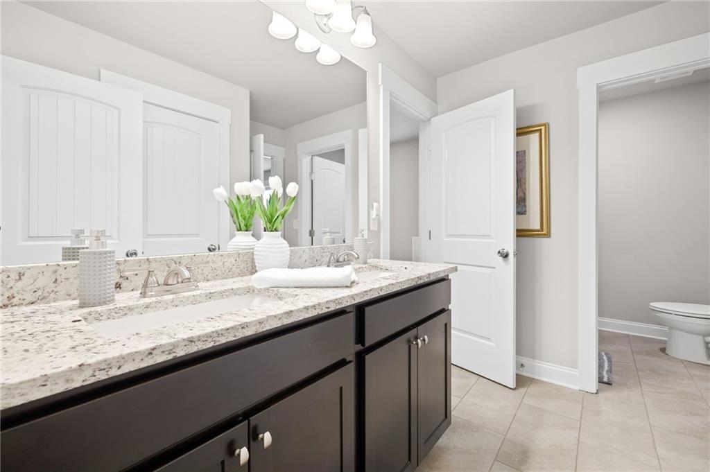 2440 Traditions Way Jefferson, GA 30549 - Photo 19 of 32 a bathroom with a granite countertop sink a toilet and a mirror