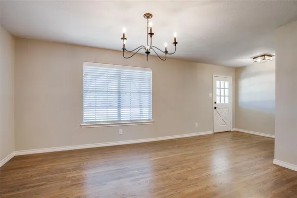 an empty room with wooden floor chandelier and windows