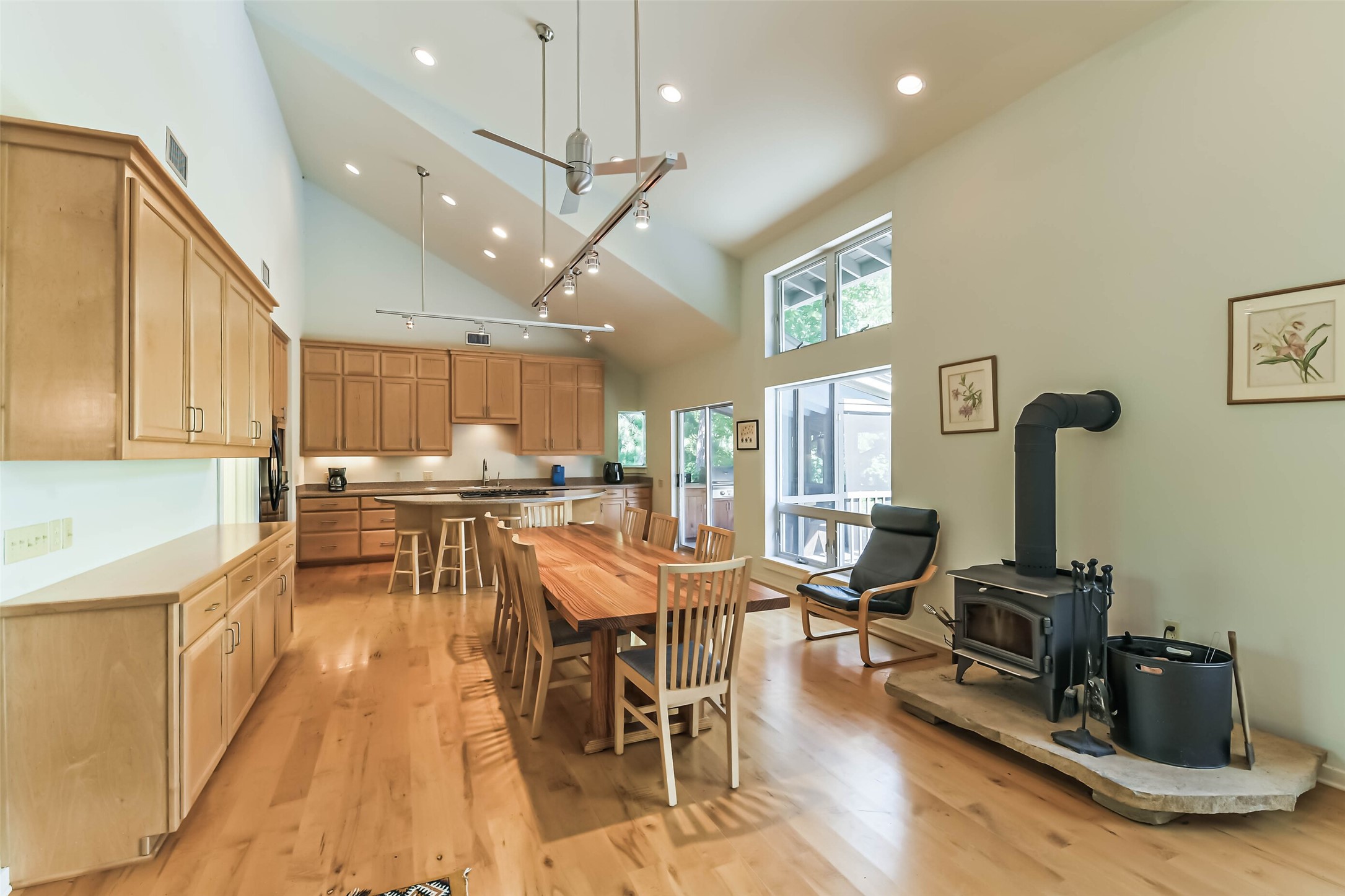 88 Raccoon Ramble Cleveland, TX 77327 - Photo 11 of 43 Spacious kitchen and dining area featuring vaulted ceilings, abundant natural light, and warm wood cabinetry. Cozy wood-burning stove adds charm next to expansive windows and a comfortable seating area.