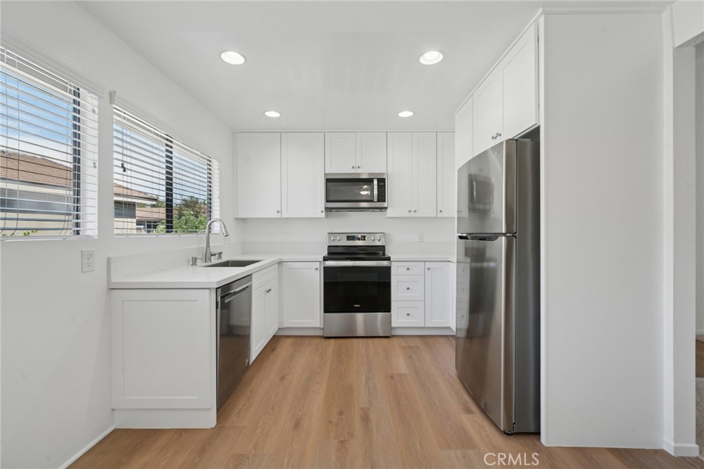 82 Streamwood Irvine, CA 92620 - Photo 2 of 26 a kitchen with a refrigerator a stove top oven a sink and dishwasher with wooden floor