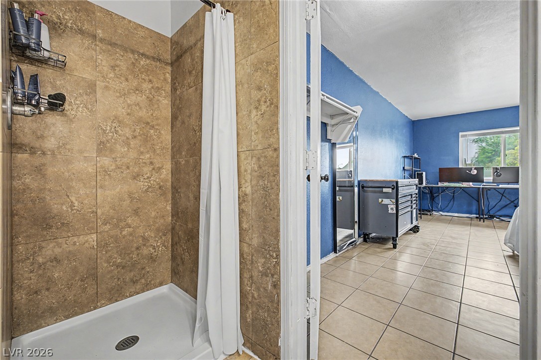 5357 Indian Wells Road Las Vegas, NV 89110 - Photo 23 of 39 A neatly tiled shower with a white curtain opens into a room featuring durable tile flooring.