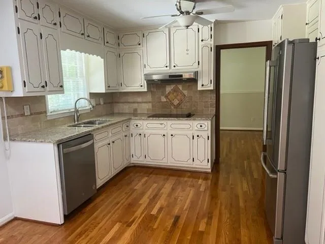 a kitchen with stainless steel appliances granite countertop a refrigerator a sink dishwasher and white cabinets with wooden floor