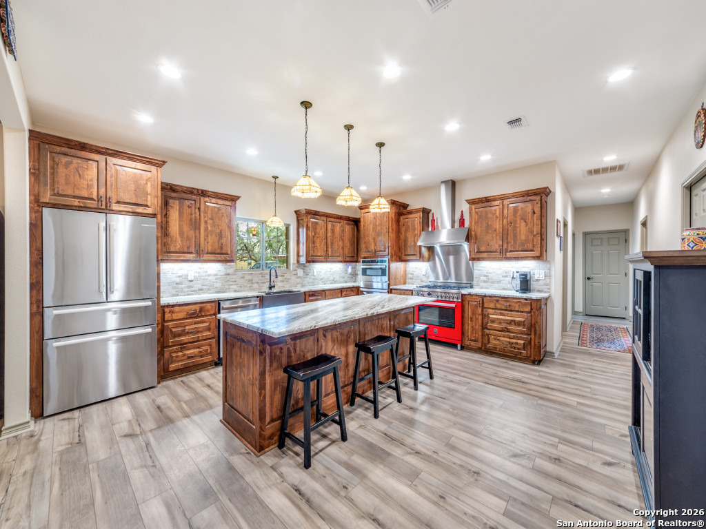 6472 Bluntzer Road Jourdanton, TX 78026 - Photo 7 of 45 a kitchen with stainless steel appliances granite countertop a kitchen island hardwood floor sink and wooden cabinets