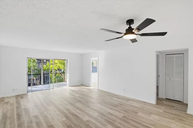 an empty room with wooden floor fan and windows
