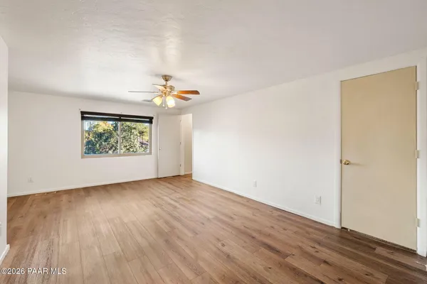 an empty room with wooden floor chandelier fan and windows