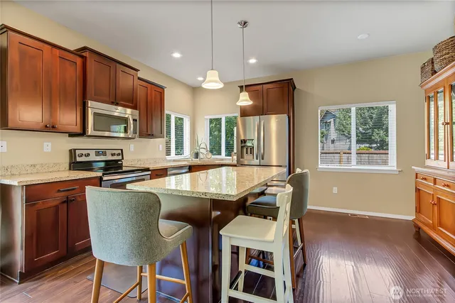 a kitchen with stainless steel appliances granite countertop wooden floors a stove a microwave a center island and a window