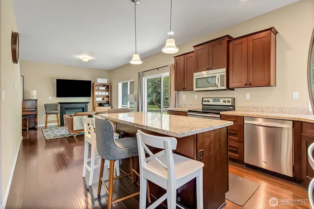 a kitchen with stainless steel appliances granite countertop a stove top oven a sink a dining table and chairs with wooden floor