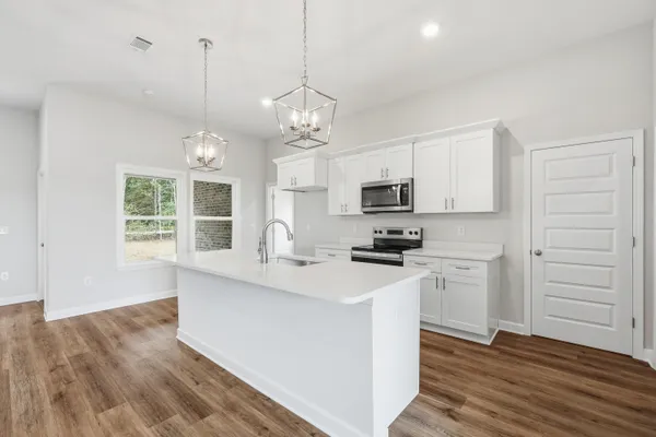 a kitchen with stainless steel appliances granite countertop a sink a stove a refrigerator and white cabinets with wooden floor