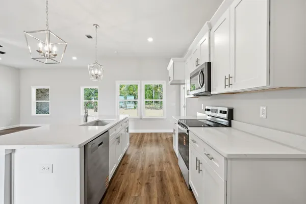 a kitchen with stainless steel appliances a stove oven a sink dishwasher and white cabinets with wooden floor