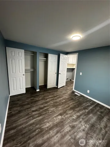 a view of an empty room with wooden floor and kitchen