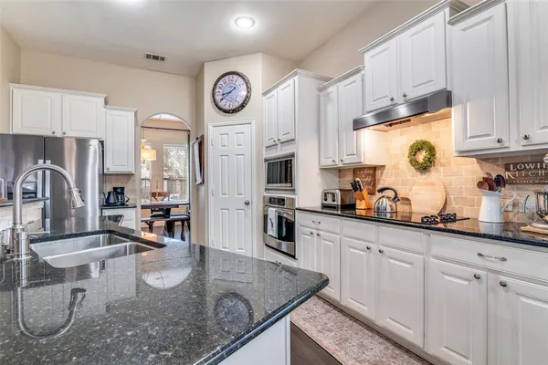 a kitchen with stainless steel appliances granite countertop a stove top oven a sink a dining table and chairs with white cabinets