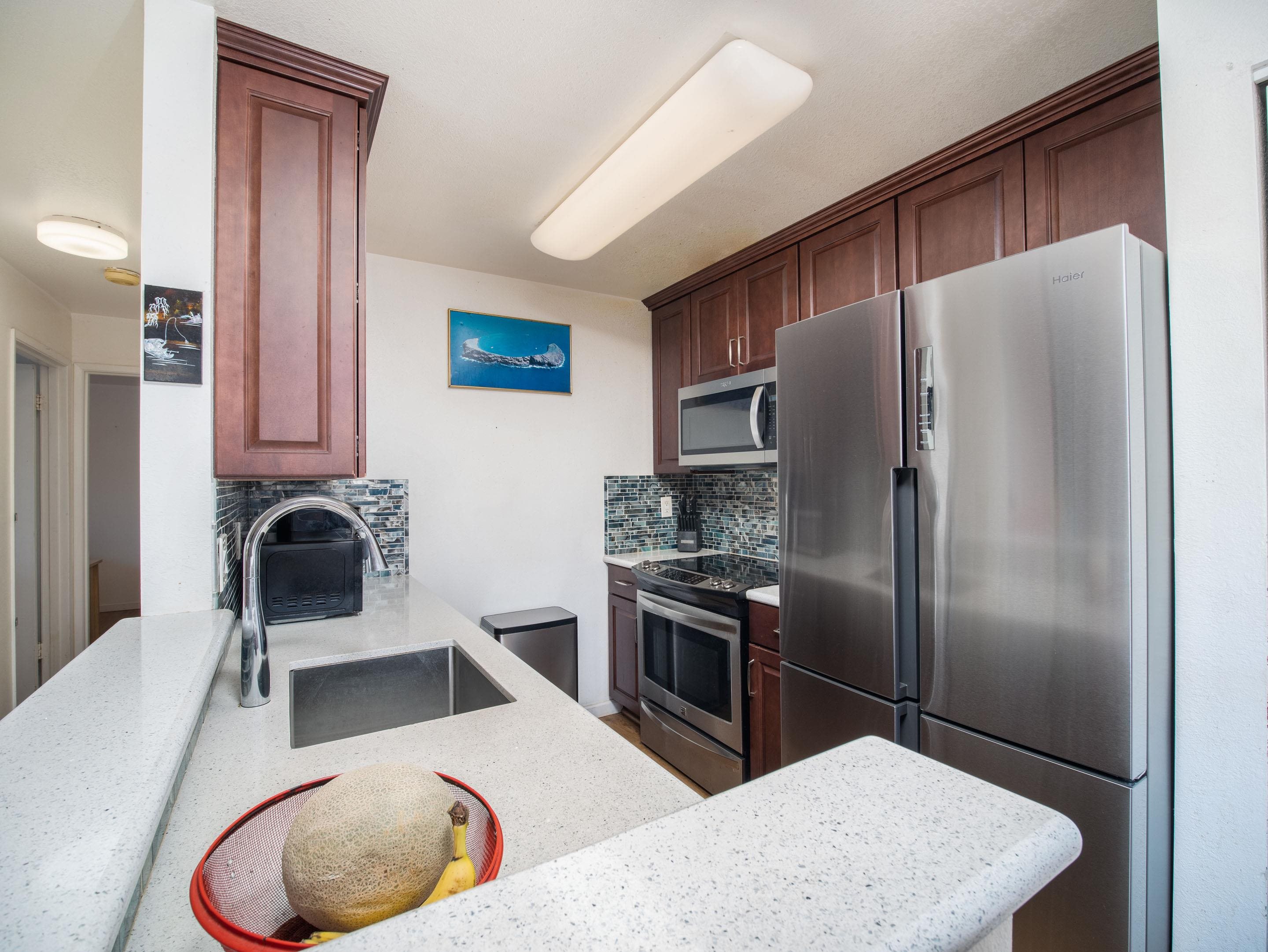 480 Kenolio Road, Unit 30206 Kihei, HI 96753 - Photo 5 of 20 a kitchen with stainless steel appliances granite countertop a refrigerator a stove and a sink with wooden floor