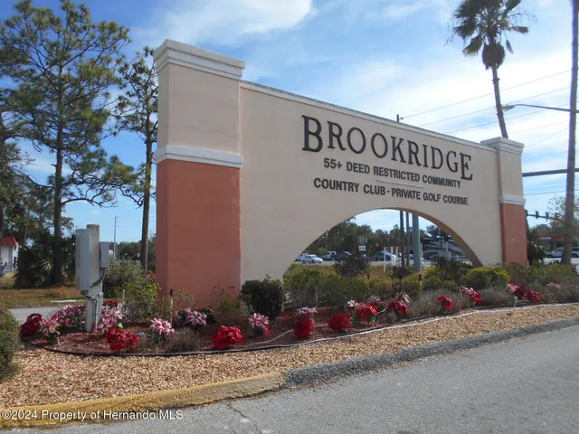 a sign board with flower plants and wooden fence