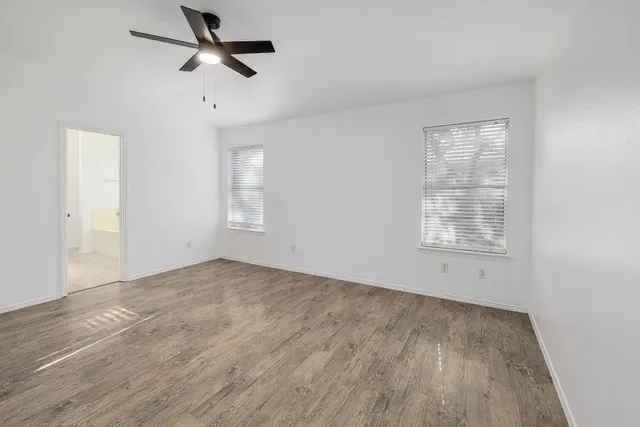 an empty room with wooden floor ceiling fan and windows