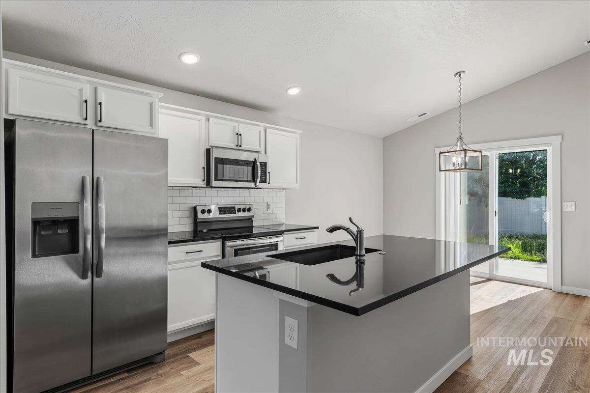 3091 S Green Boise, ID 83709 - Photo 11 of 27 Modern kitchen featuring an island with integrated sink, stainless steel appliances, white cabinetry, subway tile backsplash, and wood-finish flooring