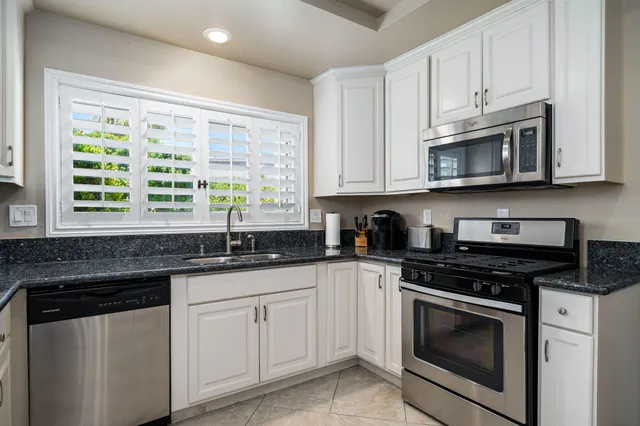 a kitchen with granite countertop white cabinets sink and stainless steel appliances