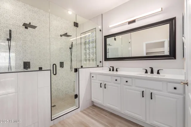 a bathroom with double vanity sink a mirror a glass door a shower and vanity