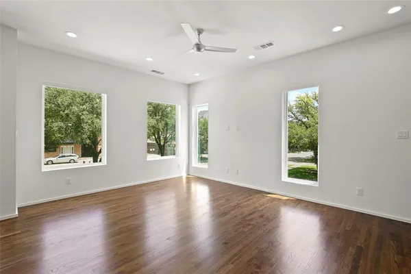 an empty room with wooden floor a ceiling fan and windows