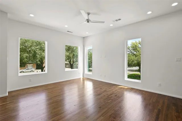 an empty room with wooden floor a ceiling fan and windows