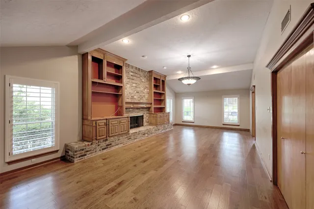 an empty room with wooden floor fireplace and windows
