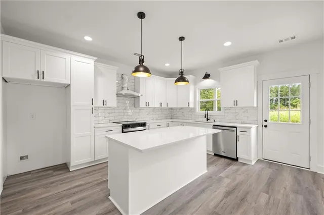 a kitchen with stainless steel appliances granite countertop a sink a stove a refrigerator and island with wooden floor