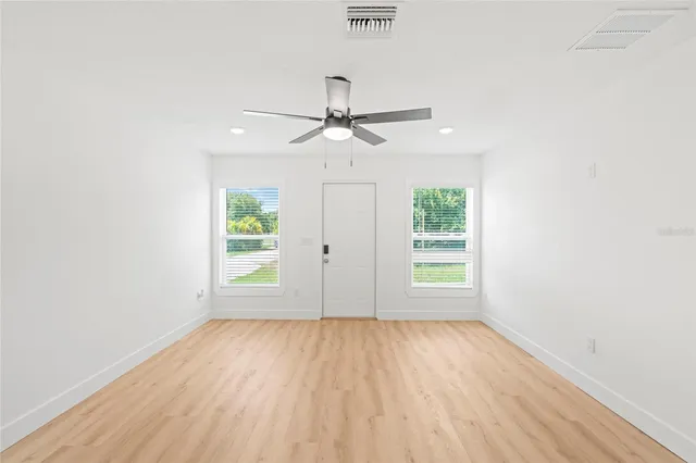 an empty room with wooden floor chandelier fan and windows