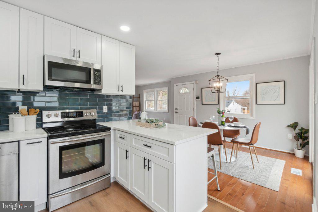 18 Rollwin Road Baltimore, MD 21244 - Photo 12 of 27 a kitchen with stainless steel appliances kitchen island granite countertop a stove top oven a sink a dining table and chairs with white cabinets