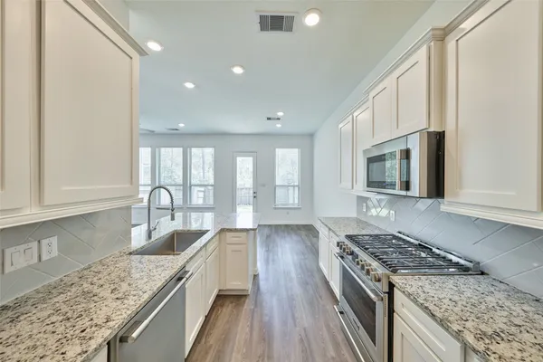 a kitchen with granite countertop a refrigerator a sink a stove and white cabinets with wooden floor