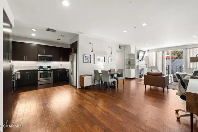 a kitchen with stainless steel appliances granite countertop a stove top oven a sink a dining table and chairs with wooden floor