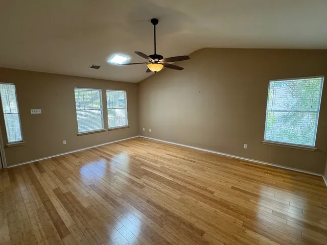 an empty room with wooden floor chandelier fan and windows