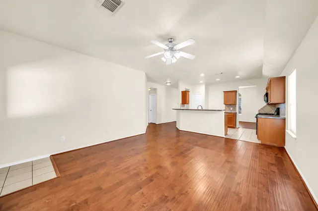 a view of an empty room with wooden floor and a kitchen