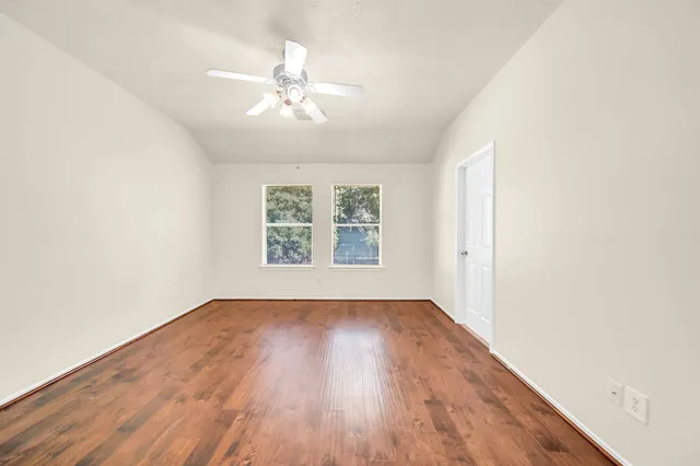 an empty room with wooden floor chandelier fan and windows