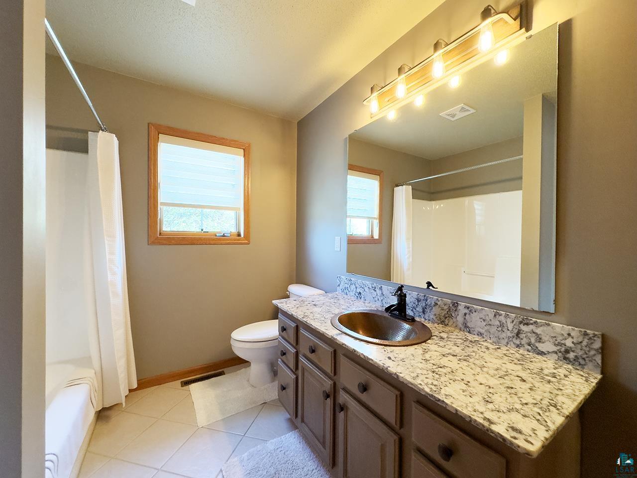 197 Jefferson Street Buhl, MN 55713 - Photo 14 of 31 Bathroom with toilet, vanity, baseboards, tile patterned flooring, and shower / bath combo