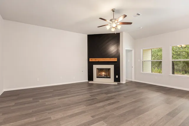 a view of an empty room with wooden floor fireplace and a window