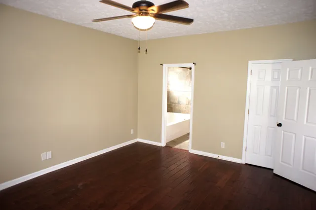 an empty room with wooden floor fan and windows