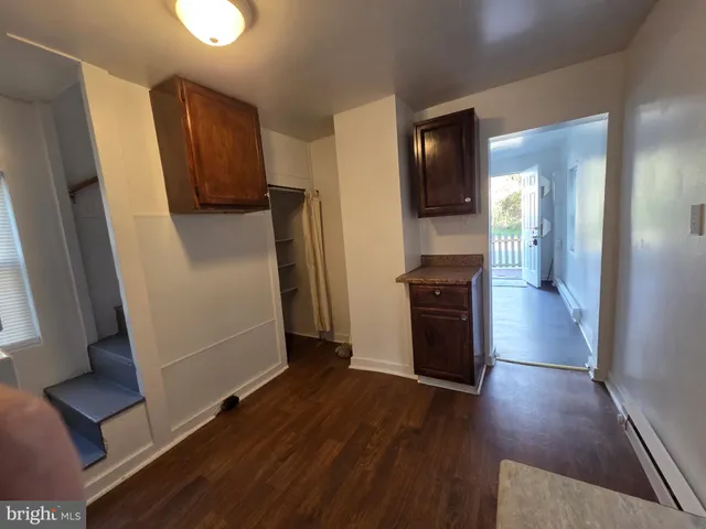 a view of a refrigerator in kitchen and an empty room with wooden floor