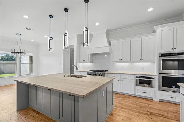 a kitchen with stainless steel appliances granite countertop a stove a sink a refrigerator and white cabinets with wooden floor