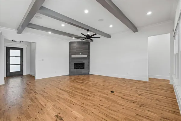 a view of an empty room with wooden floor and a kitchen