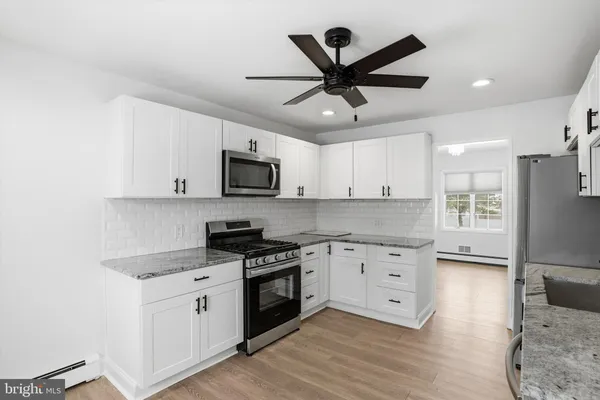 a kitchen with granite countertop a refrigerator a sink a stove and white cabinets