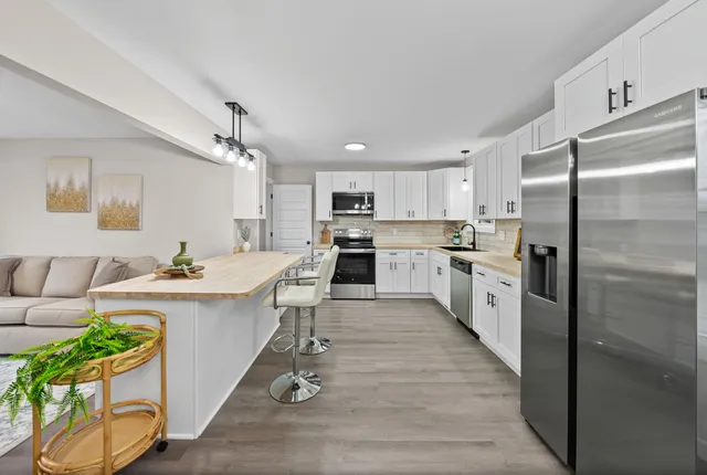 a large kitchen with kitchen island a island a stove a sink dishwasher a refrigerator and white cabinets with wooden floor