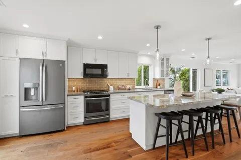 a kitchen with stainless steel appliances granite countertop a sink a stove a refrigerator and island with wooden floor