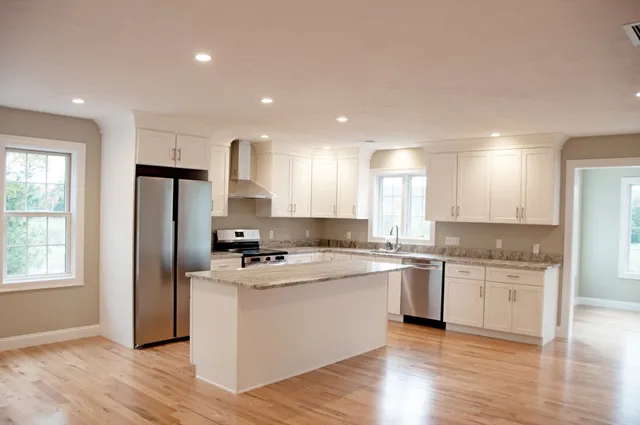 a kitchen with stainless steel appliances granite countertop a stove a sink dishwasher a refrigerator and white cabinets with wooden floor