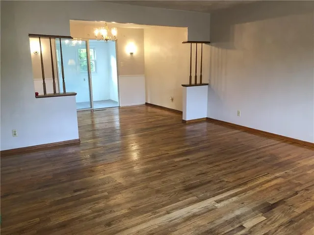 a view of empty room with wooden floor and kitchen view