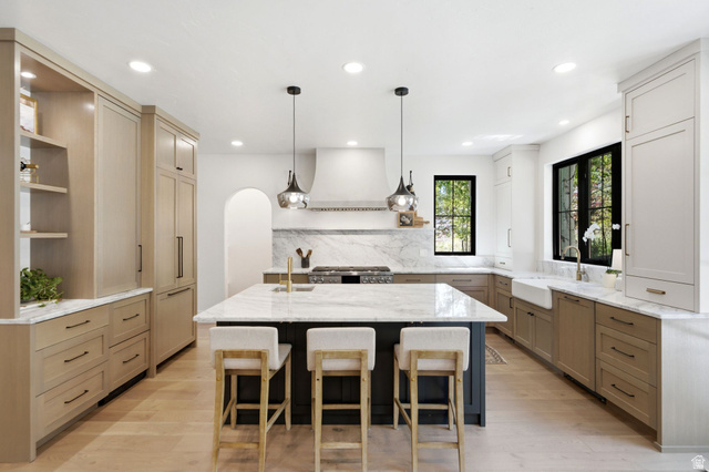 3027 Homestead Road Park City, UT 84098 - Photo 9 of 62 Spacious kitchen featuring a large central island with seating, a farmhouse sink, stainless steel appliances, marble backsplash, and light wood-finish flooring