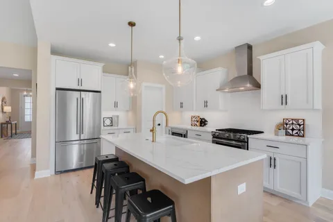 a kitchen with stainless steel appliances a stove a refrigerator a sink and white cabinets with wooden floor