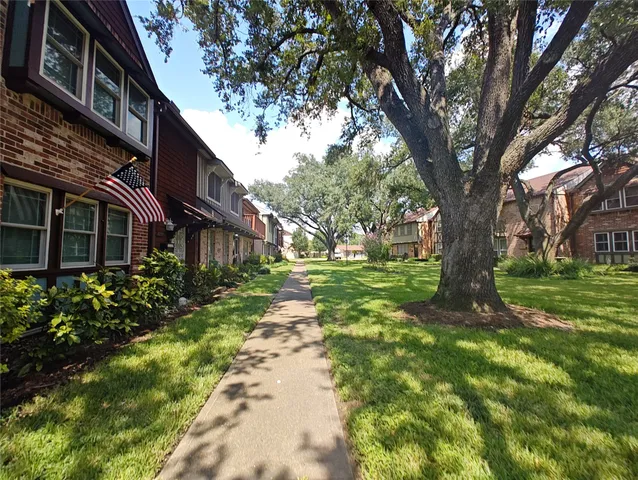 a view of a brick house with a big yard plants and large trees
