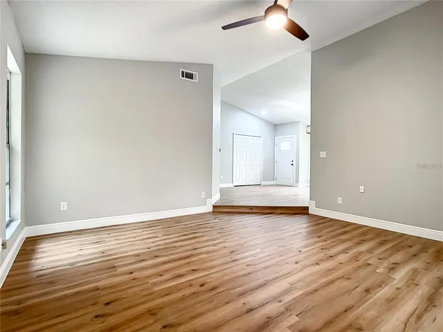 an empty room with wooden floor chandelier fan and windows