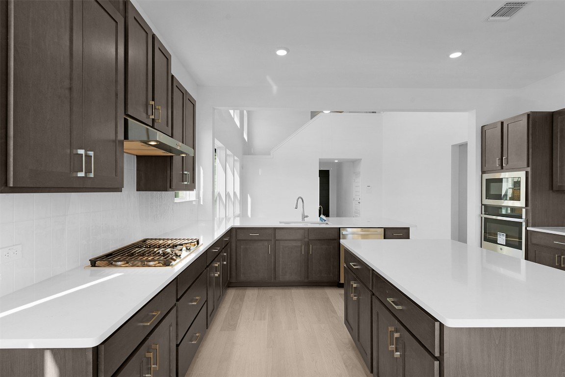 417 Raleigh Drive Georgetown, TX 78633 - Photo 7 of 29 Kitchen featuring a kitchen island, light wood-style floors, stainless steel appliances, dark brown cabinetry, and light stone countertops